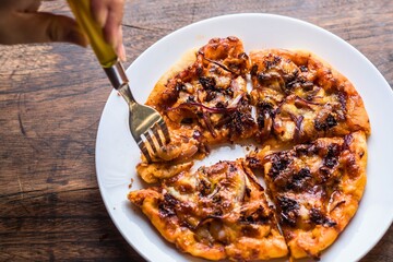 Hand using a fork to take a slice of delicious homemade pizza