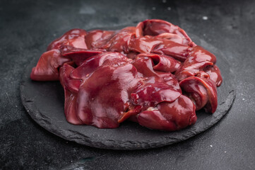 Raw chicken liver on a dark slate plate, accompanied by fresh rosemary and garlic cloves. Stylish dark background enhances the rich red hue.