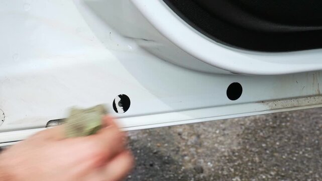 Wiping away tar from the inside of a white van door with a yellow microfiber cloth