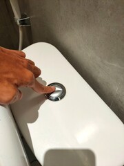 Portrait photo of a finger pressing the split chrome flush button on a white toilet tank, indicating activation of a dual-flush system.