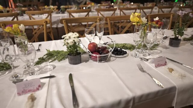Elegant wedding reception table setting with flowers, fruits, and glassware in a rustic venue.