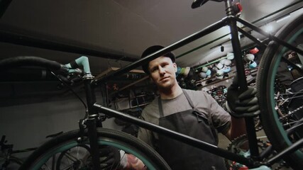 Portrait of confident Caucasian technician holding bicycle working in repair workshop, looking at camera