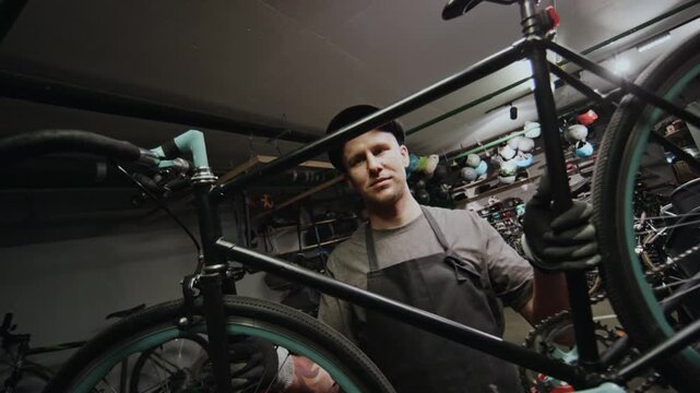 Portrait of confident Caucasian technician holding bicycle working in repair workshop, looking at camera