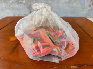 Fresh chilies in a clear plastic bag on a wooden table bought from a local market in Malang, Indonesia. Bird's eye chili.