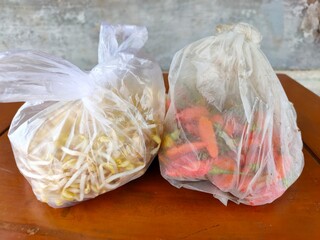 A clear plastic bag filled with fresh bean sprouts and chillies on a wooden table. Fresh produce from a local market in Malang, Indonesia.