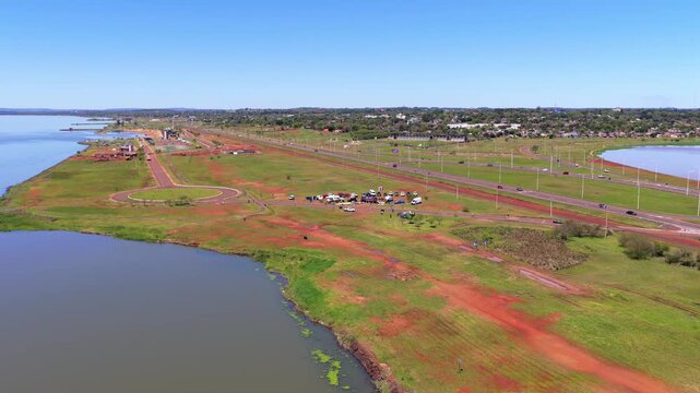 Miguel Lanus and Acceso Sur in Posadas, Misiones featuring sprawling fields bordered by the Paran&aacute; River and distinctive red earth, with roads and highways curving along the waterfront, drone shot.