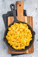 Savory baked macaroni with cheese in a skillet. Wooden board and gray surface add a cozy, stylish touch.