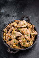 Cooked stew from poultry gizzards with herbs in cast iron pan on dark stone background perfect for rustic food photography and menu design.