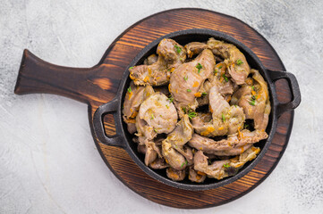 Cooked chicken gizzards with herbs in cast iron pan on white background perfect for rustic food photography and recipe design.