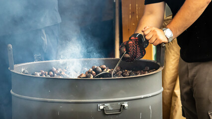 roasting chestnuts in large metal drum with smoke rising