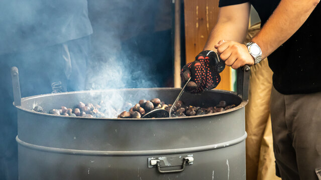 roasting chestnuts in large metal drum with smoke rising