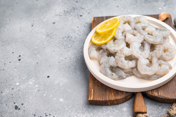 Fresh prawn shrimp tails on a wooden board. Gourmet ingredient with spices and lemon slices, ready for cooking on a rustic table.