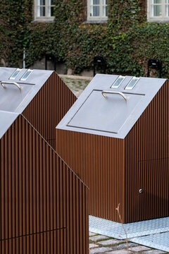 Close exterior view of an urban public waste container integrated into surrounding architecture, emphasizing functional design with sustainable ecofriendly elements and clear recycling purpose