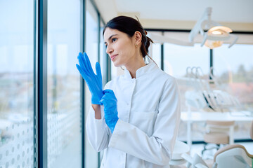 Female dentist or assistant preparing for a dental procedure by putting on blue protective gloves...