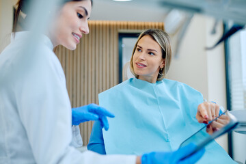 Dentist in protective gloves showing a digital tablet to a patient, discussing oral hygiene and treatment plan during a consultation