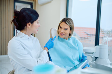 Obraz premium Dentist discussing oral health with a smiling female patient, providing dental care and professional advice in a clinic