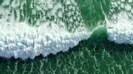 Ocean wave breaking and forming white foam on a deep green sea from above, a dynamic aerial view of the water's surface