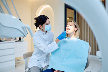 Female dentist wearing mask and gloves performing an oral checkup on a woman in a modern dental clinic