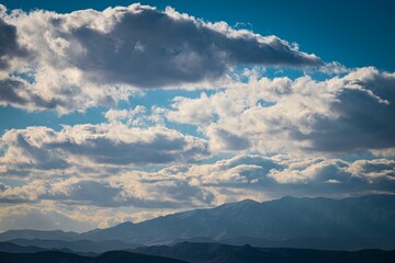 Dramatic sky filled with thick, textured clouds over a distant mountain range on a clear day