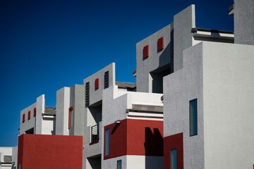 Modern architectural detail of a residential building with geometric shapes and contrasting red and white colors against a clear blue sky