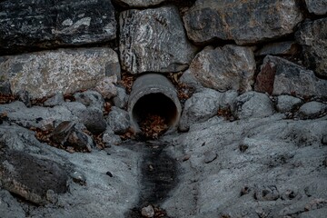 Close-up view of a stone drainage pipe outlet surrounded by natural rocks and flowing water in a rustic outdoor setting