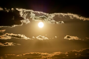 Dramatic golden sunset with sun shining through dark clouds creating a moody and atmospheric sky scene