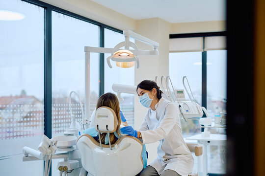 Dentistry professional in a mask and gloves preparing to examine a female patient in a modern dental office