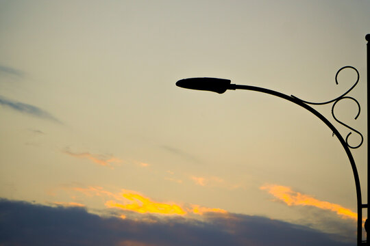 sunset in the park. A classic lamppost glowing warmly against a moody, cloudy evening sky. A classic lamppost glowing warmly against a moody, cloudy evening sky.Close-up of a glowing street lamp at du