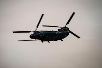 Military heavy-lift tandem rotor helicopter flying in the sky during dusk with silhouette effect showcasing aviation technology and defense capabilities
