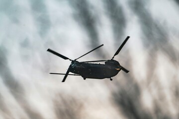 Silhouette of a military helicopter flying against a cloudy sky, showcasing aviation and defense technology in action
