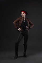 Steampunk fashion: woman with bright red hair in goggles and hat on dark gray