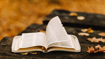 Open Bible on a wooden surface with autumn leaves and a blurred background