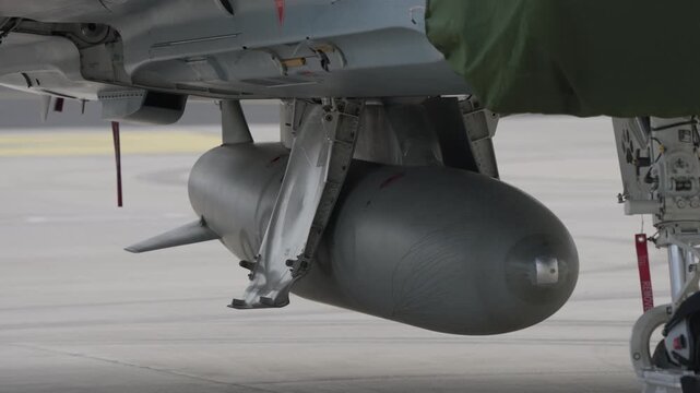 Close up of electronic pod mounted under fighter jet fuselage with landing gear and safety tags visible