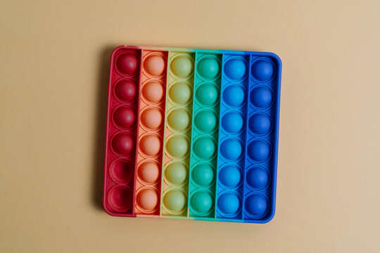Rainbow Pop It Sensory Toy for Stress Relief and Focus in Children.Rainbow-colored silicone Pop It sensory toy placed on a beige background. Designed to reduce stress, support focus