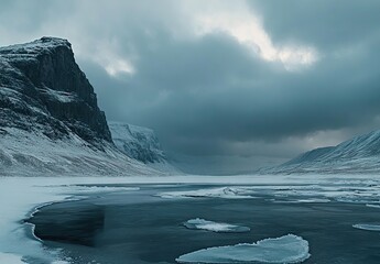 A frozen river winding through snow-covered mountains under a dramatic cloudy sky at dawn
