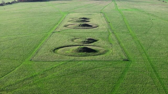 Aerial shot reversing away from row of huge burial mounds near Stonehenge
