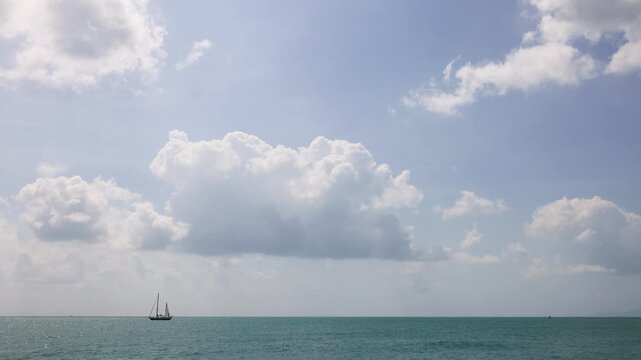 Tropical sea timelapse with sailboats on the horizon, bright turquoise water, and large cumulus clouds moving across a clear blue sky. The scene evokes calmness, freedom, and the beauty of nature in m