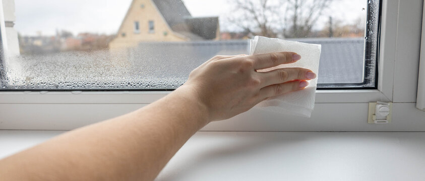 Woman's hand wiping condensation and water drops from a foggy window with a paper towel