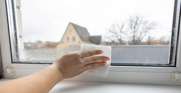 Woman's hand wiping condensation and water drops from a foggy window with a paper towel