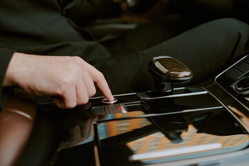 Caucasian young adult man pressing button on modern car center console, hand and part of arm visible, engaging with vehicle controls, interior reflecting cityscape in glossy surface