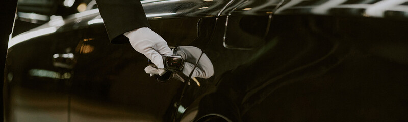 Caucasian middle aged man wearing glove opening car door with hand visible, luxury vehicle reflecting surroundings, professional chauffeur service concept, closeup focus