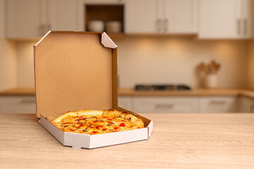 Freshly baked pizza in open cardboard box on wooden kitchen table, warm lighting and soft background ideal for food delivery and restaurant promotion