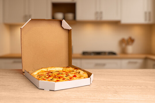 Freshly baked pizza in open cardboard box on wooden kitchen table, warm lighting and soft background ideal for food delivery and restaurant promotion