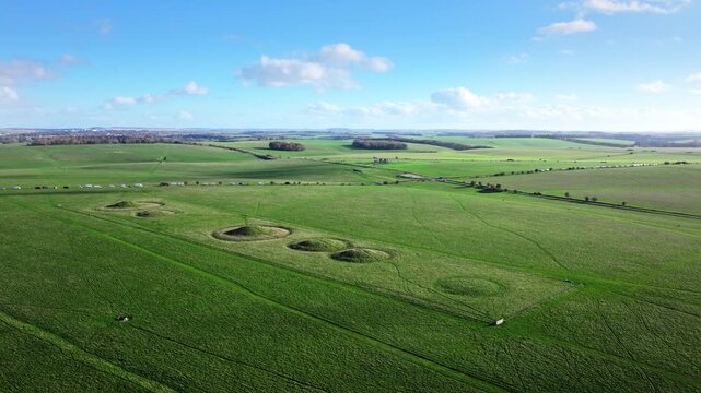 Aerial shot flying low over a row of burial mounds with Stonehenge in the distance