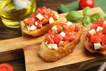 Tasty bruschettas with tomatoes, mozzarella cheese and basil served on wooden table, closeup