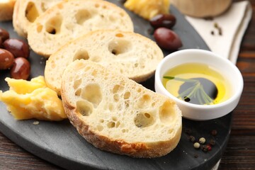 Pieces of fresh ciabatta, oil, olives, peppercorns and cheese on wooden table, closeup