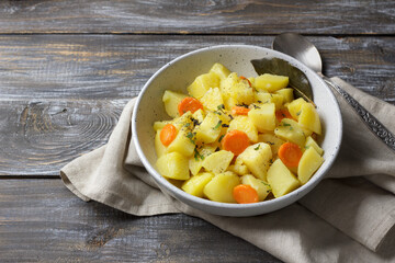 Rustic homemade stew with tender potatoes and carrots served in a ceramic bowl on wooden table. Warm comfort food with herbs and spices, natural light and cozy texture