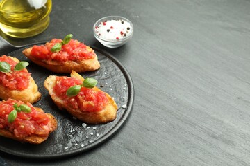 Tasty bruschettas with tomatoes and basil served on black table, closeup. Space for text