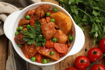 Delicious cooked stew in bowl and ingredients on wooden table, flat lay