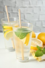 Fototapeta premium Refreshing water with lemons and mint on white marble table, closeup